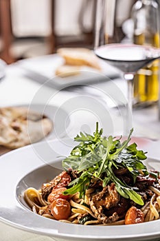 Detail of meat linguine with tomatoes and rocket served with wine on a cafeteria table