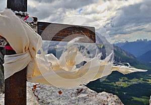 Metallic cross detail with white scarf and small white cross on the mountain peak top - mountains and clouds are in the background photo