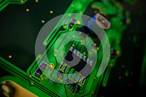 Detail of a microprocessor, resistors and capacitors soldered to a green glowing PCB