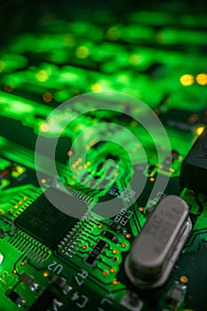 Detail of a microprocessor, resistors and capacitors soldered to a green glowing PCB