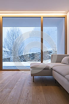 Detail of modern sofa in living room with large windows, view of nature and snow