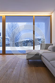 Detail of modern sofa in living room with large windows, view of nature and snow