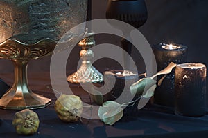 Detail of mysterious looking still life with handmade burning candles and stabilized dried leaves and pomegranates
