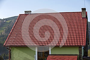 Detail of new modern house cottage corner with stucco walls decorated with natural stones, red shingled roof and rain gutter pipe
