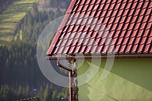 Detail of new modern house cottage corner with stucco walls decorated with natural stones, red shingled roof and rain gutter pipe