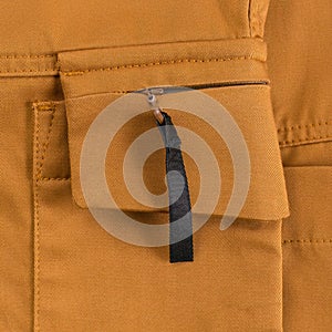 Detail of ocher colored cargo pants. Zipped side pocket with black tab