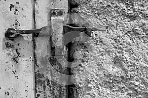 Detail of an old cellar door with a rusted latch next to rough plaster in b/w