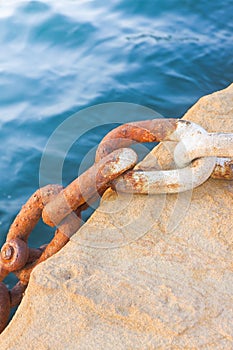 Detail of an old rusty metal chain anchored to a concrete block