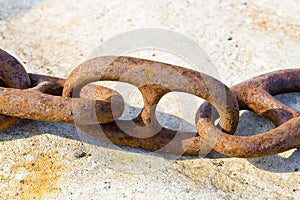 Detail of an old rusty metal chain anchored to a concrete block