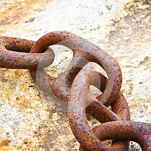 Detail of an old rusty metal chain anchored to a concrete block