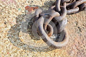 Detail of an old rusty metal chain anchored to a concrete block