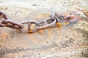 Detail of an old rusty metal chain anchored to a concrete block