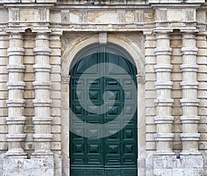 Detail of an old urban building stone facade with tall green wood door and decorative columns