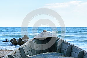 Detail of old wooden boat on beach sand with blurry blue water sea in the background