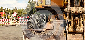 Detail on old yellow digger machine back, road closed signs, construction in progress background. Roadworks concept banner