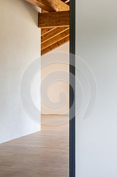 Detail of an open door, empty white room with exposed wood beams and hardwood floors