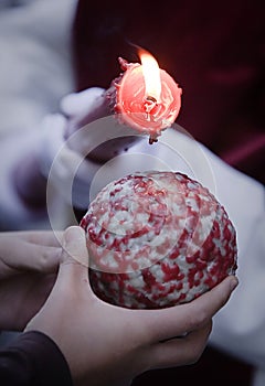 Detail penitent red holding a candle pouring wax on a ball that holds a child in the hand during Holy Week