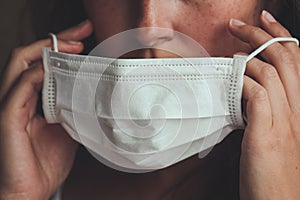 Detail photo of unrecognizable white woman putting on a white medical face mask to prevent the flu. Blurred background, focus on