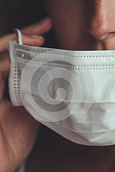 Detail photo of unrecognizable white woman putting on a white medical face mask to prevent the flu. Blurred background, focus on