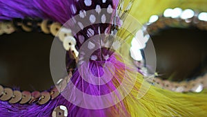 Detail of pink and yellow feather carnival domino mask with green feather outline and golden jewellry decorations