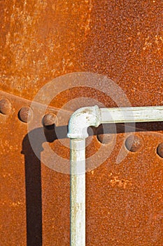 Detail of a pipeline against a rusty riveted metal tank