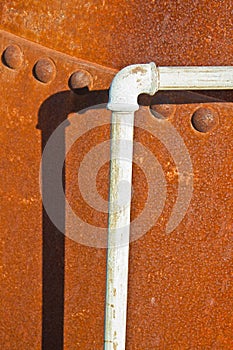 Detail of a pipeline against a rusty riveted metal tank