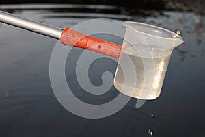 Detail of plastic sampling beaker on rod with sample of water
