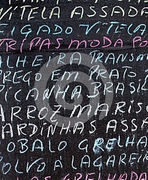 Detail of a portuguese menu written in multicolored chalk on a black chalkboard