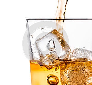 Detail of pouring scotch whiskey in glass with ice cubes on white