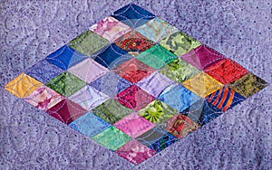 Detail of quilt sewn from multi-colored rhombus on a lilac background