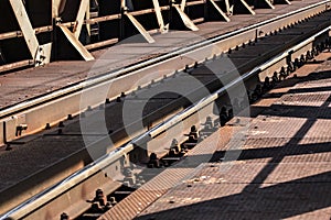 Detail of railway tracks on old metal bridge, sun casting shadow