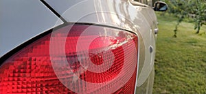 Detail of the rear end of a silver car with focus on the brake lights. Red rear light of the car. Brake signal for the