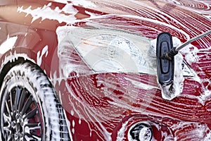 Detail on red car front light washed in self serve carwash, white soap strokes on surface