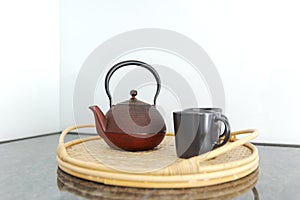 Detail of a red Chinese teapot and two black cups resting on a wicker tray, in a bright kitchen