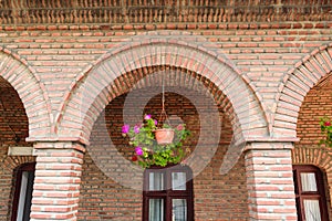 Detail of red vintage brick arcades, brown windows frame and hanging geranium flower pot