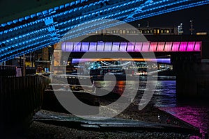 Detail of rivets and the steel structure of a London bridge underneath illuminating the banks of the River Thames with futuristic