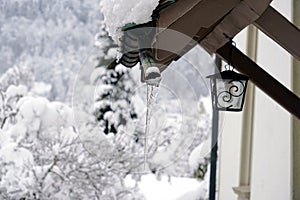 Detail of a roof of the house in winter. It is covered with snow and there is an icicle hanging down from it