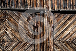 Detail of rustic old wooden barn doors of rough and weathered planks with rusted iron hinge and lock
