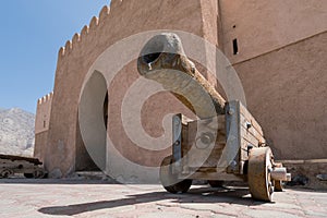 Detail of a rusty, medieval cannon with wooden wheels in front of ancient arab fort in Bukha, Oman.