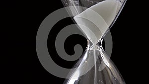 Detail of sand pouring in hourglass on black background, time passing concept