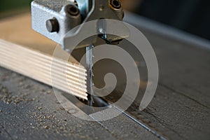 Detail of the saw blade of an electric bandsaw and a multiplex wood panel in a workshop, copy space, selected focus, narrow depth photo