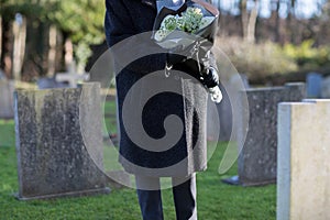 Close Up Of Senior Woman With Flowers Standing By Grave