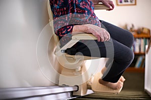 Detail Of Senior Woman Sitting On Stair Lift At Home To Help Mobility