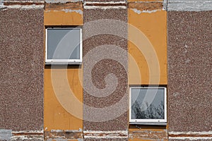 Detail of a shabby prefabricated concrete house brown wall with two decorative windows and vertical orange lines, close-up,