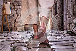 Detail shot of female legs wearing comfortable travel sandals walking on old medieval cobblestones street dring