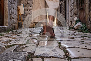 Detail shot of female legs wearing comfortable travel sandals walking on old medieval cobblestones street dring photo