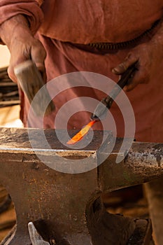 Detail shot of the hands of a blacksmith as he hammers on the red hot tip of a metal bar