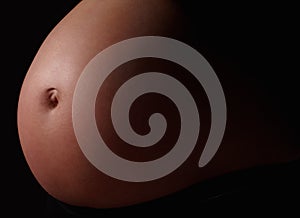 Detail shot of a pregnant womans belly against black. Belly of a pregnant woman against black background.