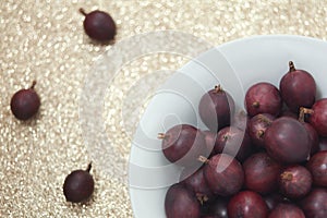 Detail shot of red gooseberries in a bowl on a glittering golden background.