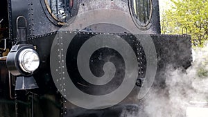 Detail shot of steam train engine with smoke. Black train composition, waiting on a station.